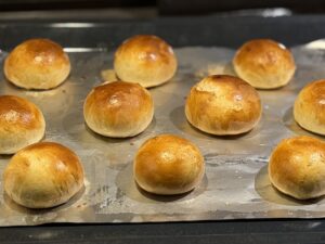 Golden brown Shrove buns cooling on a baking tray before filling